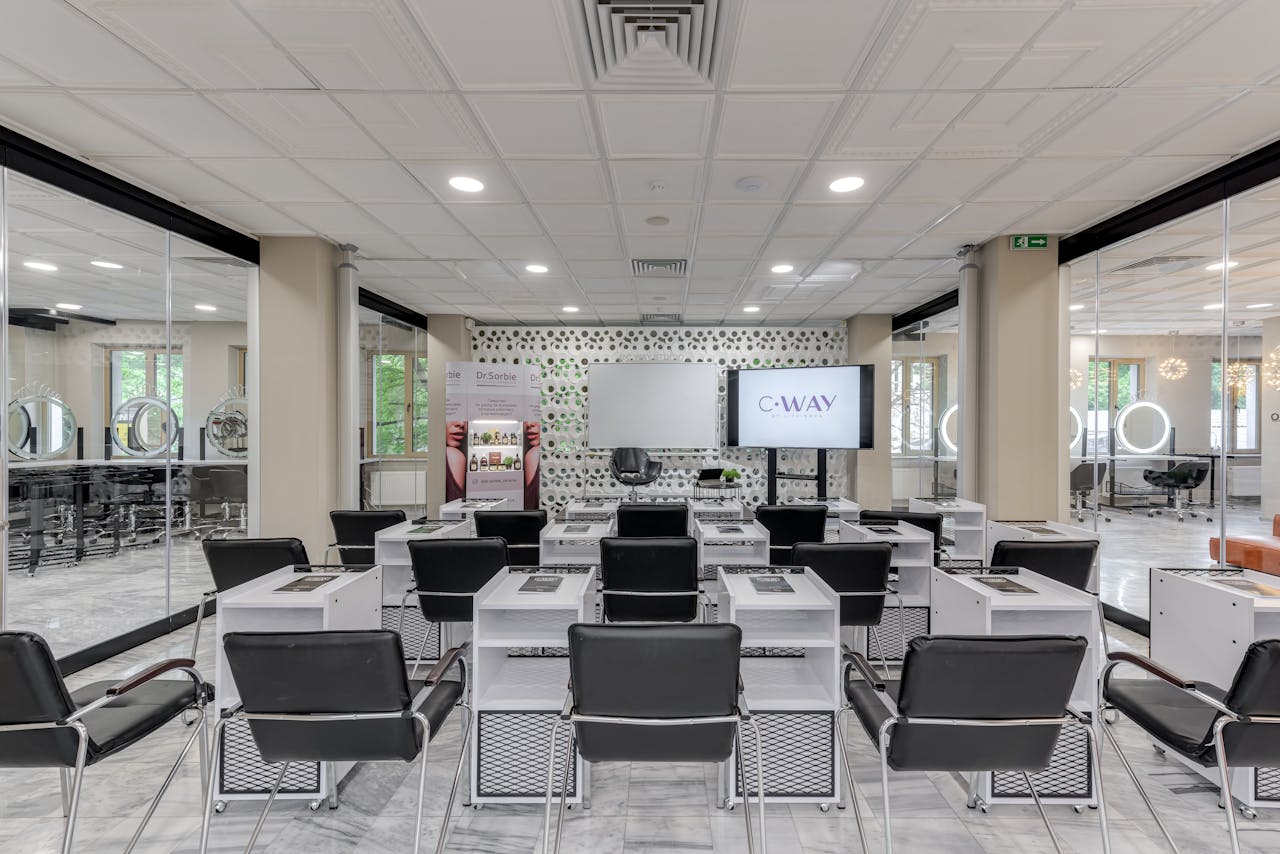 Bright and modern hair salon training area featuring rows of black chairs and equipped desks.