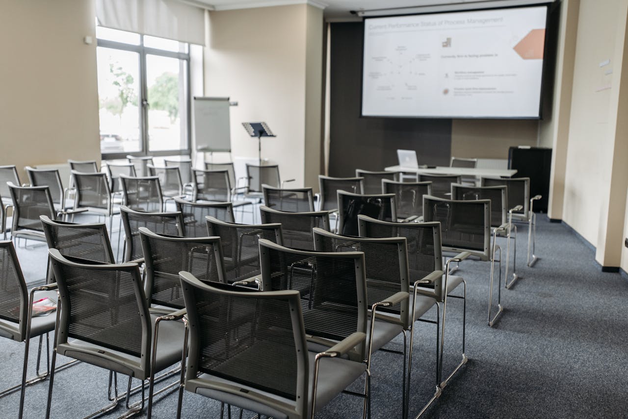 Spacious empty conference room with arranged chairs, screen, and natural light for professional meetings.