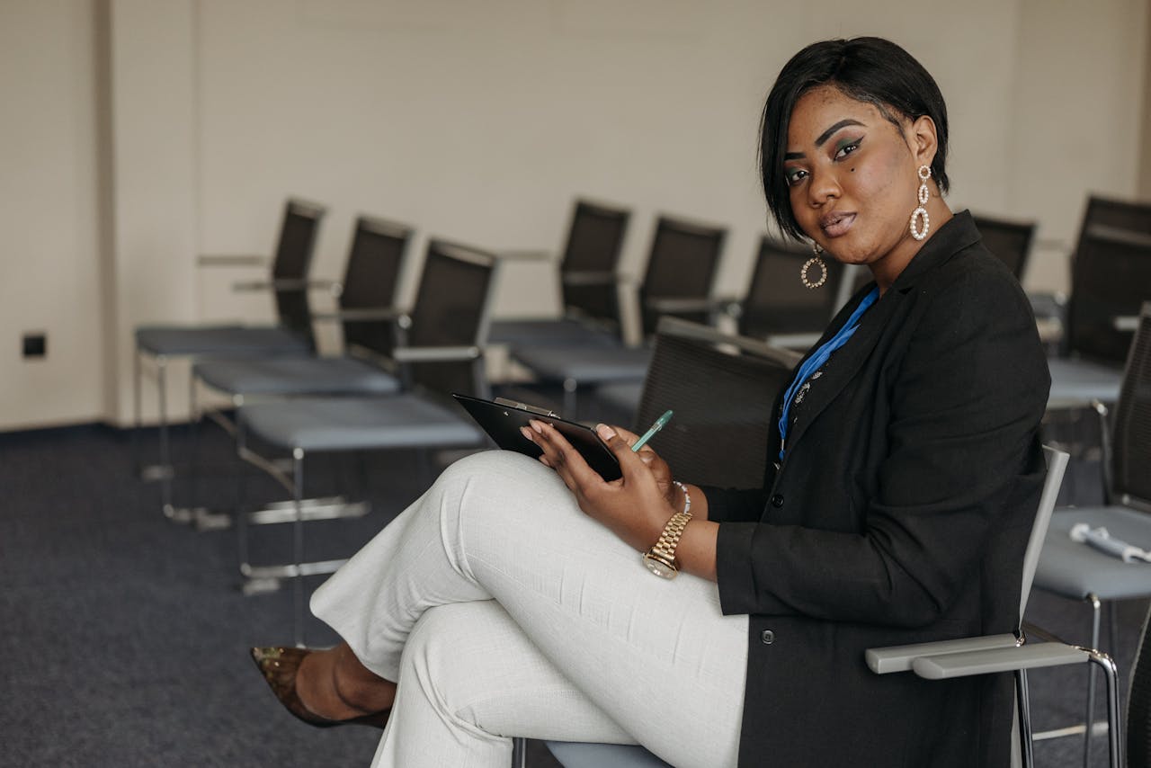 African American woman in business attire sitting in a meeting room holding a clipboard.